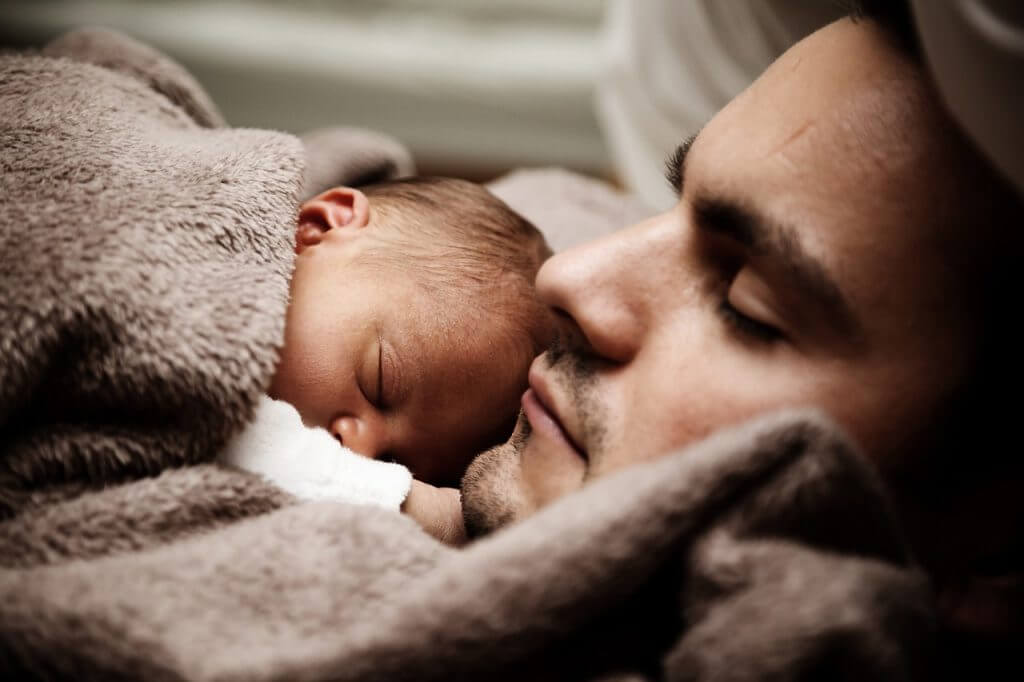 Père dormant avec son bébé dans les bras.