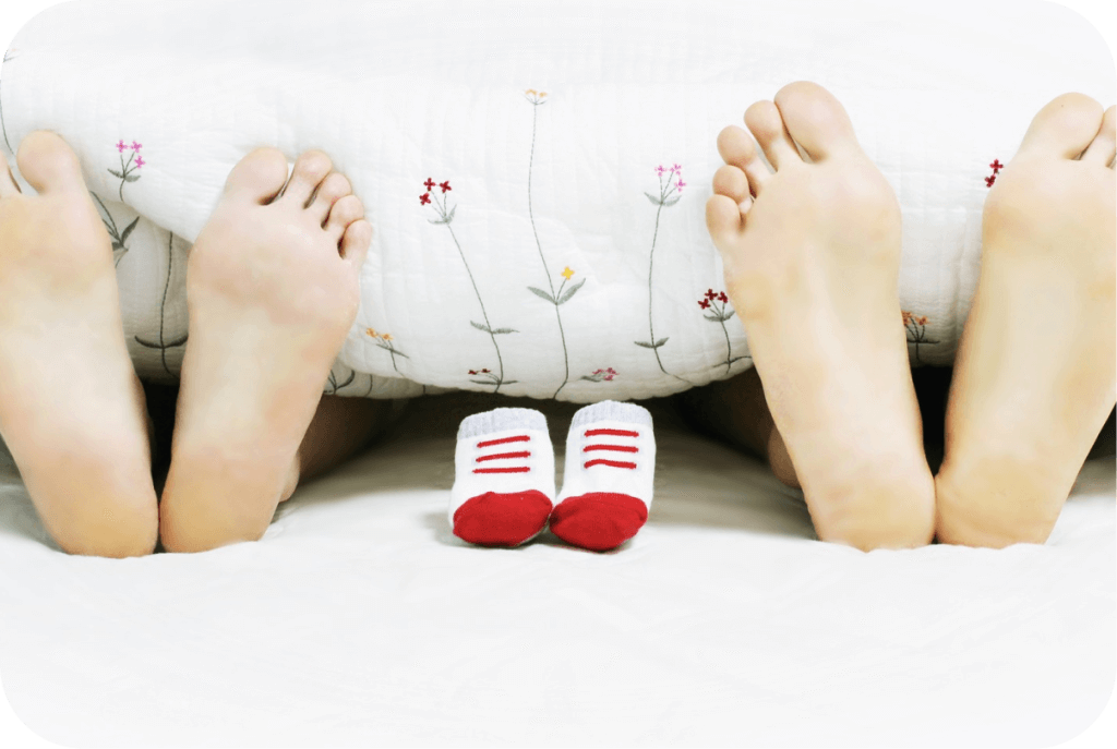 Photo de pieds de parents dépassant du lit avec des chaussons du futur bébé